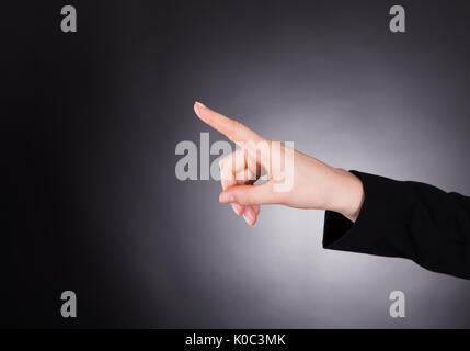Cropped image of young businesswoman touching transparent screen against black background Stock Photo