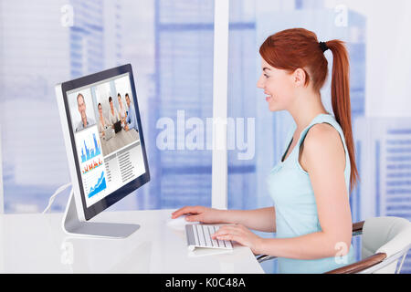 Side view of young businesswoman video conferencing with team on computer at desk in office Stock Photo