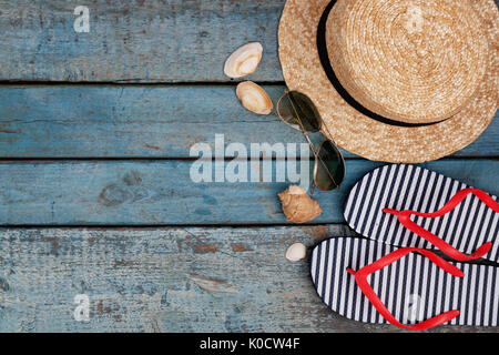 Still life of different items for relaxing on the beach, rubber flip-flops, hat, camera, phone, sunglasses, headset on a wooden blue background. Conce Stock Photo