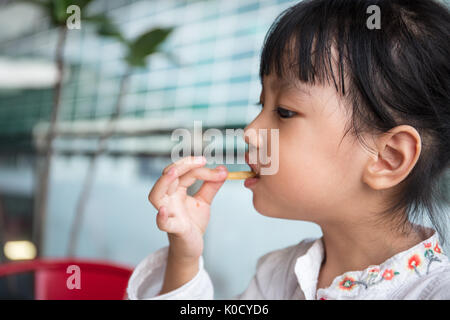 Asian Chinese little girl eating French Fries at outdoor cafe Stock Photo