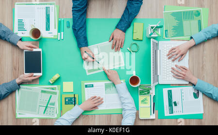 Business people working together on a green desktop and examining a report; environment, green business and finance concept Stock Photo