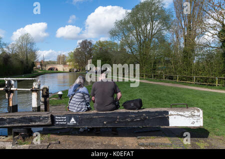 Couple sitting on some lock gates, enjoying the afternoon sunshine; Grand Union Canal, Stoke Bruerne, Northamptonshire, UK Stock Photo