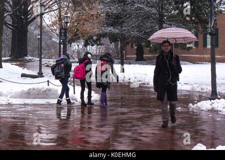 A male graduate student holding an umbrella walks towards the camera as three female undergraduate students in warm clothes and snow boots walk behind him in the opposite direction while it is raining and several inches of snow cover the ground, located between the Freshman Quad and Keyser Quad at Johns Hopkins University, Baltimore, Maryland, December 10, 2013. Courtesy Eric Chen. Stock Photo