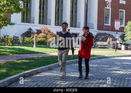 One male and one female college student holding drink and food take a stroll down the cobble stone driveway in front of the Milton S Eisenhower Library at Johns Hopkins University, smiling on a sunny day; bicycles and other students can be seen behind them on the grass in front of the library's entrance; Baltimore, Maryland, March, 2014. Courtesy Eric Chen. Stock Photo