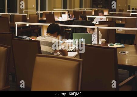 College students seated at study tables work from notebooks and laptops during the late hours of the night, the only light in the dim room coming from lamps on the tables, Albert Hutzler Reading Room, Brody Learning Commons, Johns Hopkins University, Baltimore, Maryland, March, 2014. Courtesy Eric Chen. Stock Photo