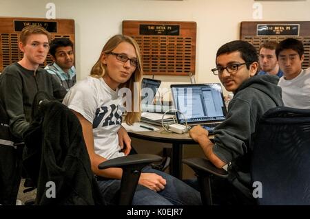 A group of male students and one female student seated at a table with laptops and notebooks turns around to pose for a photograph in the library, seemingly annoyed that their studying was interrupted, Johns Hopkins University, Baltimore, Maryland, 2014. Courtesy Eric Chen. Stock Photo