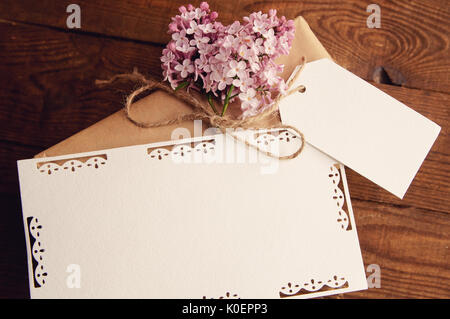 Gift wrapped with kraft paper on a wooden table, tied with a rope, with a bouquet of pink lilac, attached greeting cards Stock Photo