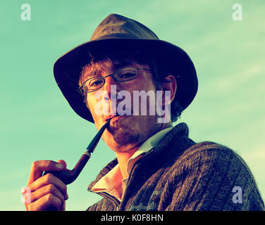 Colorized vintage outdoor portrait of man in hat smoking tobacco-pipe Stock Photo