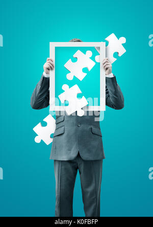 A puzzled businessman holding up a frame with puzzle pieces, business concept. Stock Photo