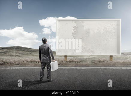 A business man standing and staring at a blank billboard advertisement.