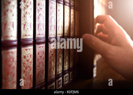 Professional library manager picking up an encyclopedia book from the shelve in a dark room. Back light and empty copy space for Editor's text. Stock Photo