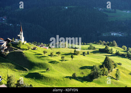 Chapel and sheep on the meadow. Bell tower, trees, shrubs and hilly green grassland. Heiliger Antoniuse church and houses in the evening light. Pitbur Stock Photo