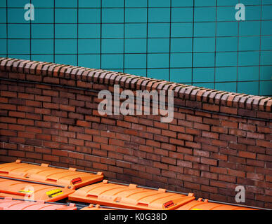 curved red brick wall behind orange waste bins with blue tiled wall in the background in Sheffield, West Yorkshire, England UK Stock Photo
