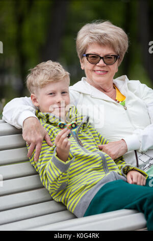 Young grandson showing new spinner gadget, happy senior grandma hugging boy on bench in park Stock Photo