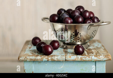 Ripe plums in a colander on a wooden background. Selective focus. Stock Photo
