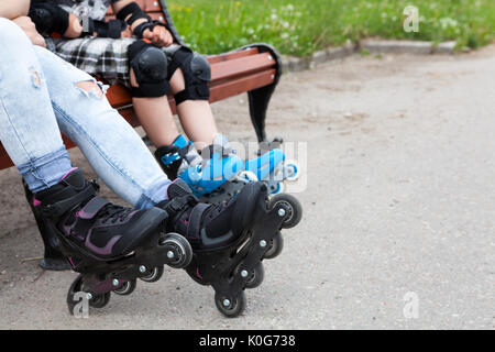 Close up view at the roller-skates wearing on female and boy legs, people sitting on the bench Stock Photo