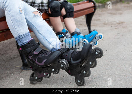 Close-up view at the in-line skates wearing on mother and children legs, people sitting on the bench Stock Photo