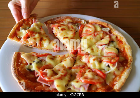 Woman's hand taking slice of ham and tomato pizza from a white plate Stock Photo