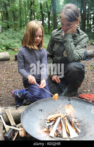 girl and her mum toast chocolate bread over a fire pit in woods in a forest school near Charlbury. U.K. Stock Photo