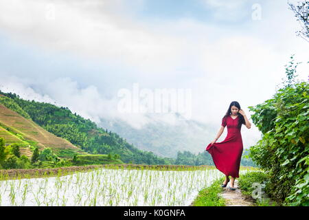 Girl in red dress walking by the rice terrace above clouds Stock Photo