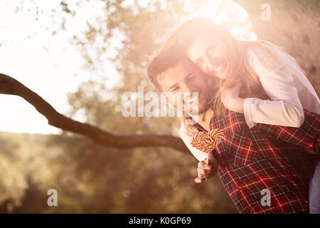Portrait of smiling handsome man giving piggy back to his girlfriend in the nature