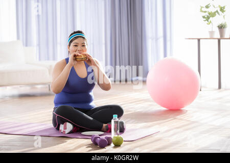Young fat woman eating during exercise Stock Photo