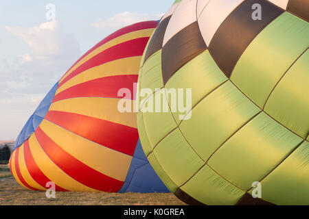 Two colorful balloons being inflated at sunrise. The light on the red, blue and gold balloon and white, green and black balloon is golden. Stock Photo