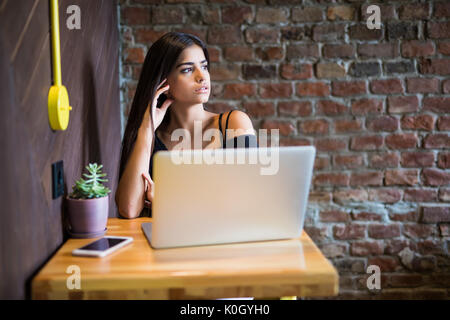 Beautiful Caucasian woman dreaming about something while sitting with portable net-book in modern cafe bar, young charming female freelancer thinking  Stock Photo