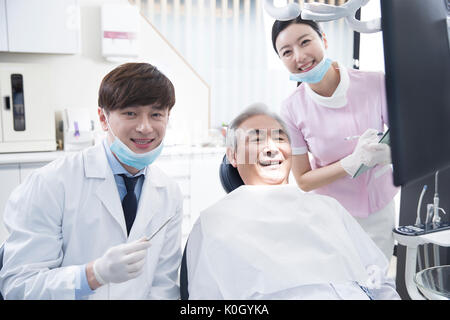 Smiling dentist and dental hygienist posing with senior male patient Stock Photo