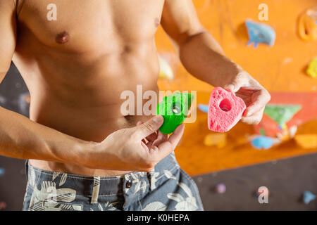 Rock climber demonstrating new bolt-on climbing holds while standing against wall in indoor climbing gym Stock Photo