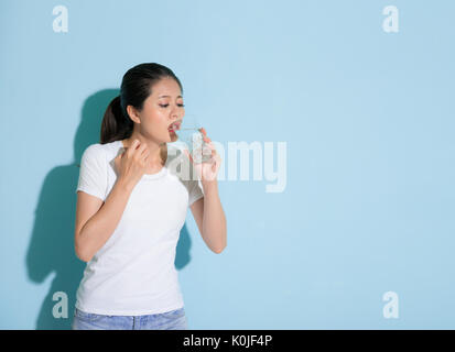 young beautiful female student drinking ice water and worry about sensitive dental problems attack standing on blue wall background. Stock Photo