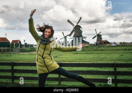 Young woman blows the wind in front of Authentic Zaandam mills in Zaanstad village on the river Zaan. Landmark of Netherlands. Stock Photo