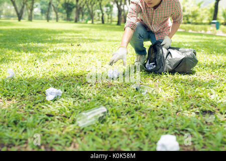 Young man crouching to waste and picking it up in bin bag Stock Photo