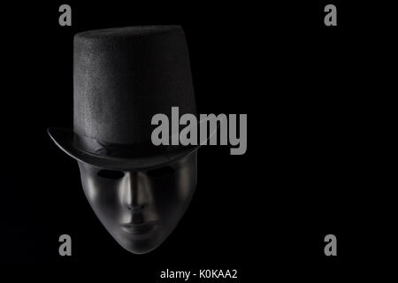 Black mask face wearing black top hat isolated on black background with copy space Stock Photo