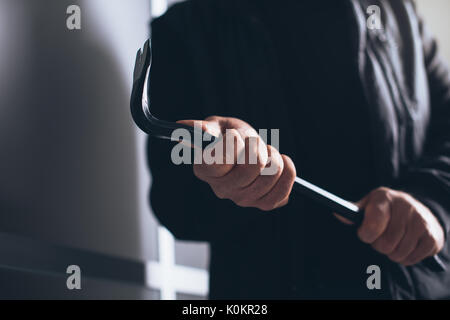 Dangerous burglar using a crowbar to break into a house late at night, home safety concept Stock Photo