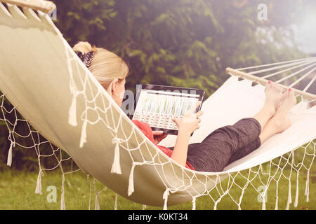 Businesswoman working on a tablet and relaxing in her garden on a hammock (vintage effect) Stock Photo