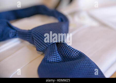 Blue silk necktie tied in a Windsor knot, resting on a white shirt in preparation for a formal event, job interview, or as part of office attire Stock Photo