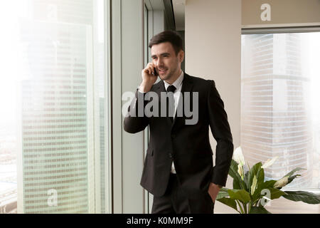 Happy businessman talking on cell standing near big office windo Stock Photo