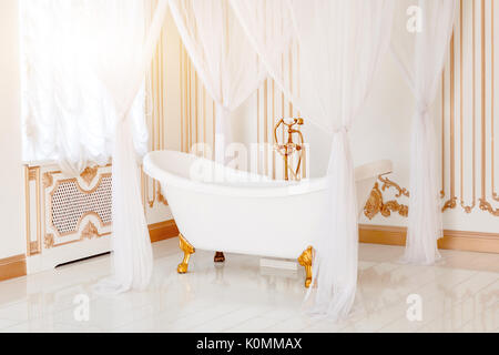 Luxury bathroom in light colors with golden furniture details and canopy. Elegant classic interior. Stock Photo