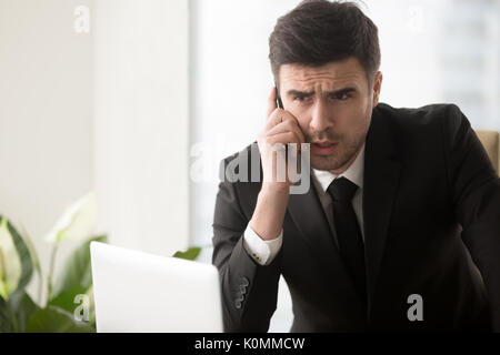 Serious worried businessman talking on phone in office, solving  Stock Photo