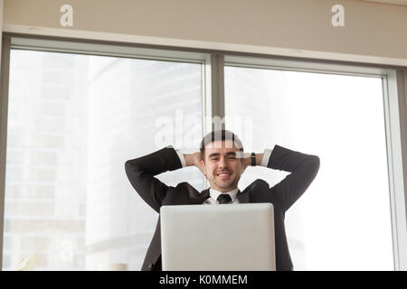 Relaxed happy businessman sitting hands behind head looking at l Stock Photo