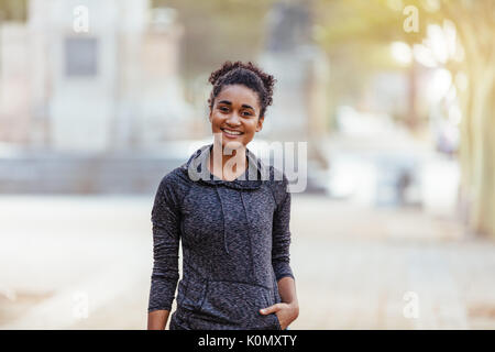 Smiling young woman in curly hair posing for a photograph. Woman in sweatshirt outdoors. Stock Photo