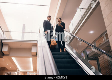 Business man and woman moving down with baggage on the escalator at the airport. Business travelers at airport. Stock Photo