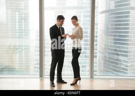 Two employees talking, using digital tablet, standing at big win Stock Photo