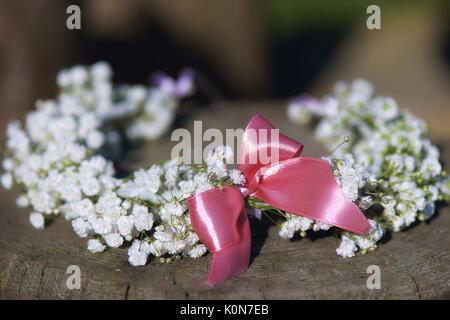 Bridal flower crown of baby's breath with small pink bow set on a tree stump, rustic minimalist wedding theme with shallow depth of field Stock Photo