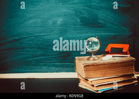 Old blackboard with chalk, books, a globe and a pencil. A beautiful backdrop for education, a free space for your text. Back to school. Shallow DOF. Stock Photo