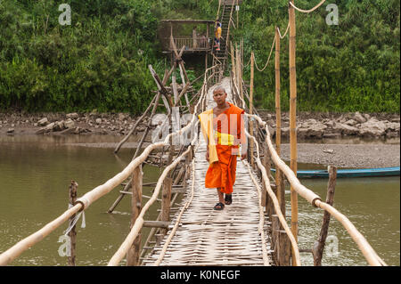 A young Buddhist monk crosses a bamboo bridge over Nam Khan river, Luang Prabang, Laos.