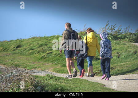 A family of holidaymakers walking along nthe coastal path in windy weather. Stock Photo