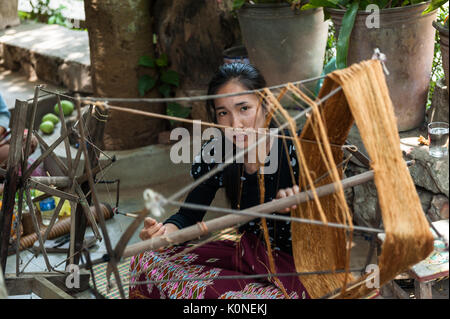 A young Lao woman spins silk yarn in Xhang Khong village. Knowledge of producing silk textiles is passed by mothers and grandmothers to girls. Stock Photo