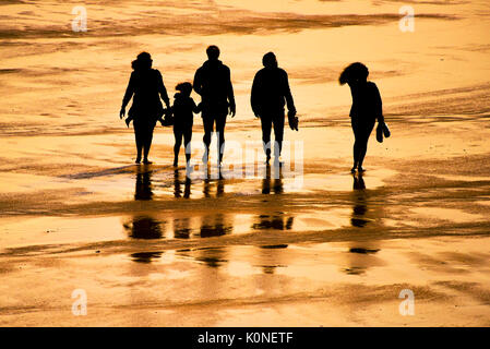 The silhouette of a family of holidaymakers walking on a beach at sunset. Stock Photo